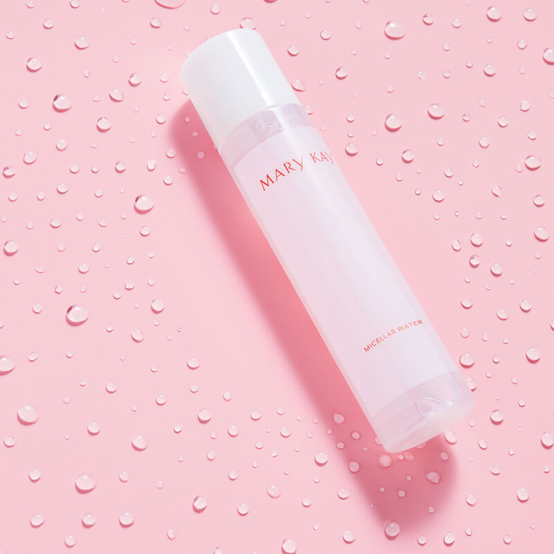 Bottle of Mary Kay Micellar Water surrounded by water droplets on pink background