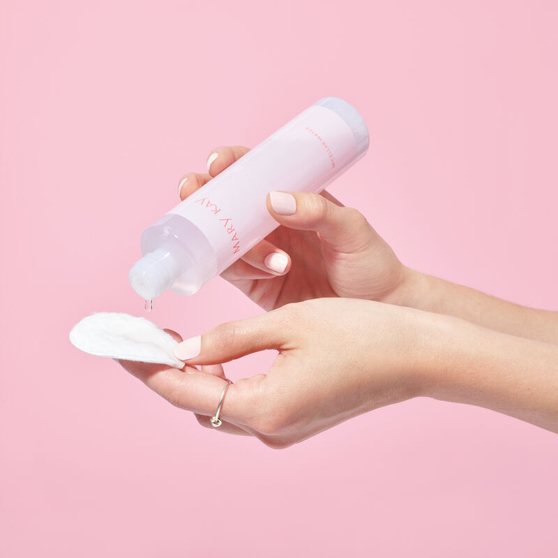 Fair-skinned hands dripping Mary Kay Micellar Water onto a cotton pad against pink background