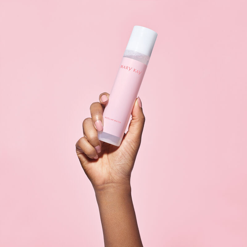 Medium-skinned hand holding bottle of Mary Kay Micellar Water on pink background
