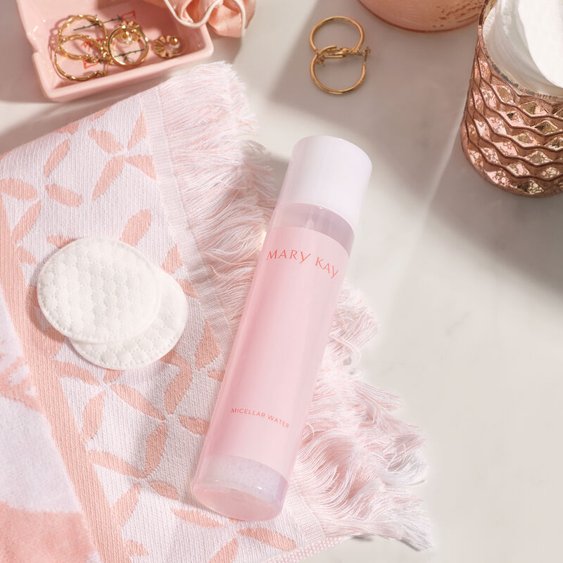 Bottle of Mary Kay Micellar Water and cotton pads laying on a pink and white patterned hand towel on white countertop
