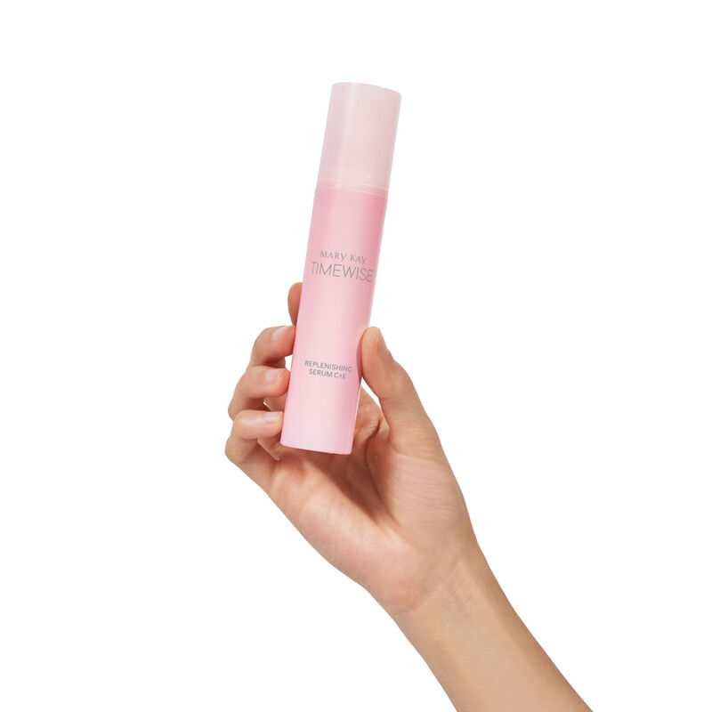 Fair-skinned hand holding pink bottle of TimeWise Replenishing Serum C+E on plain background