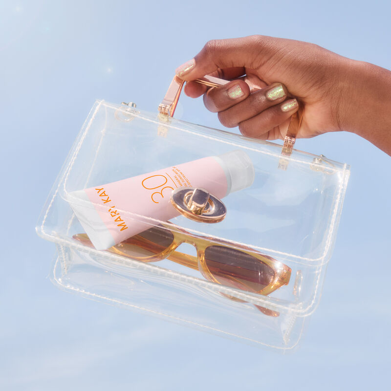 Deep-skinned hand holding a clear bag containing Mineral Facial Sunscreen SPF 30 and a pair of sunglasses