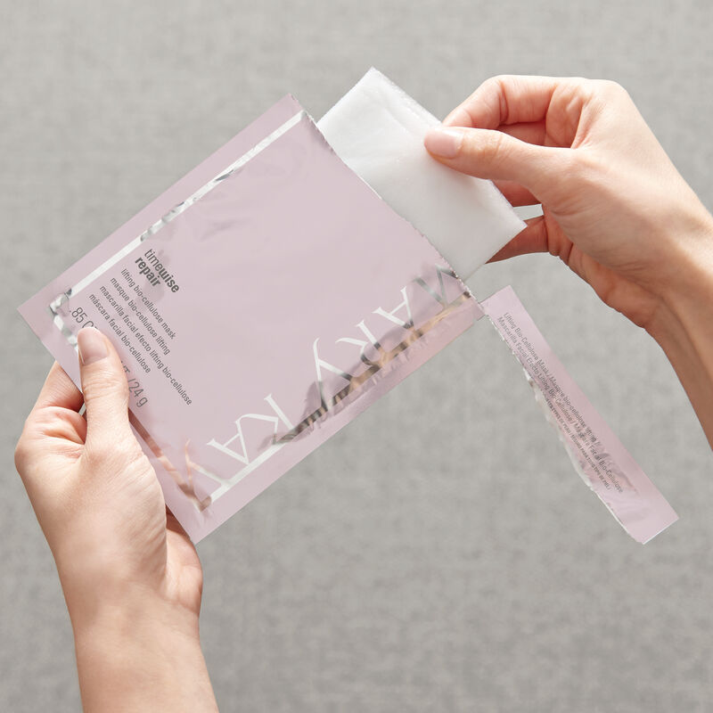 Hands removing mask from open TimeWise Repair Lifting Bio-Cellulose Mask from Mary Kay packet.