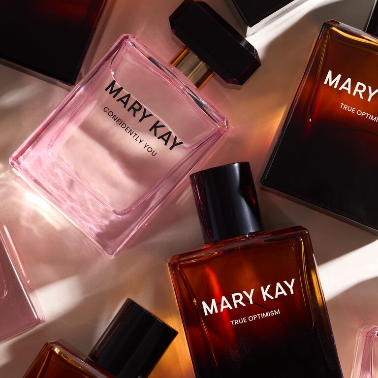 Mary Kay fragrance bottles, including &ldquo;Confidently You&rdquo; and &ldquo;True Optimism,&rdquo; arranged in warm light.