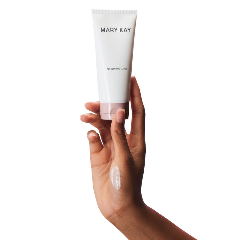 Medium-skinned hand holding up tube of Mary Kay Exfoliating Scrub against plain background