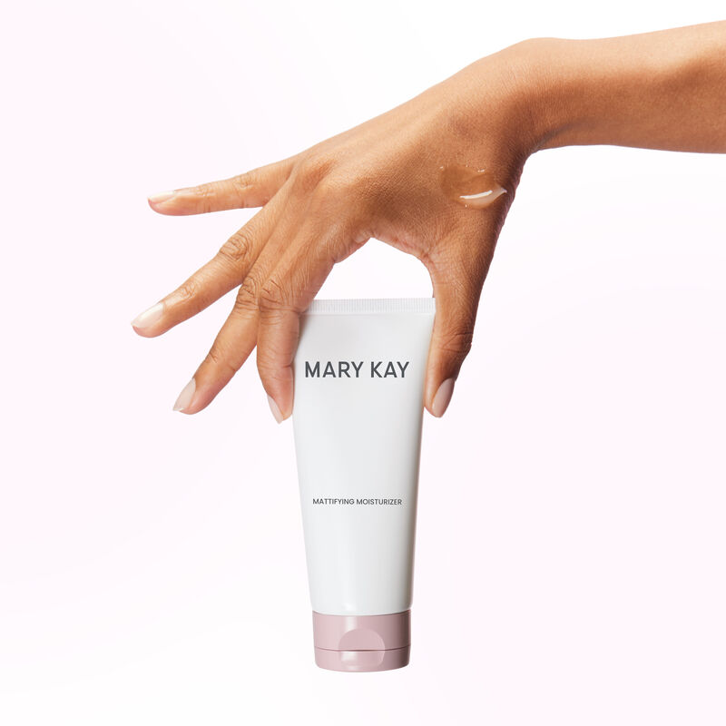 Hand with splayed fingers holding tube of Mary Kay Mattifying Moisturizer with product rub on the hand
