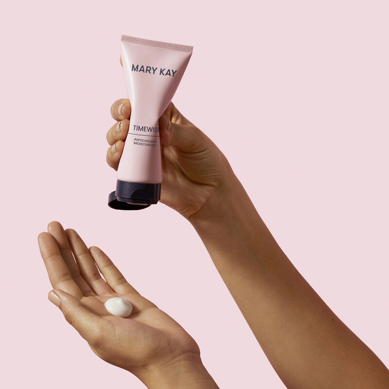 Hand squeezing dollop of TimeWise Antioxidant Moisturizer into other hand against pink background