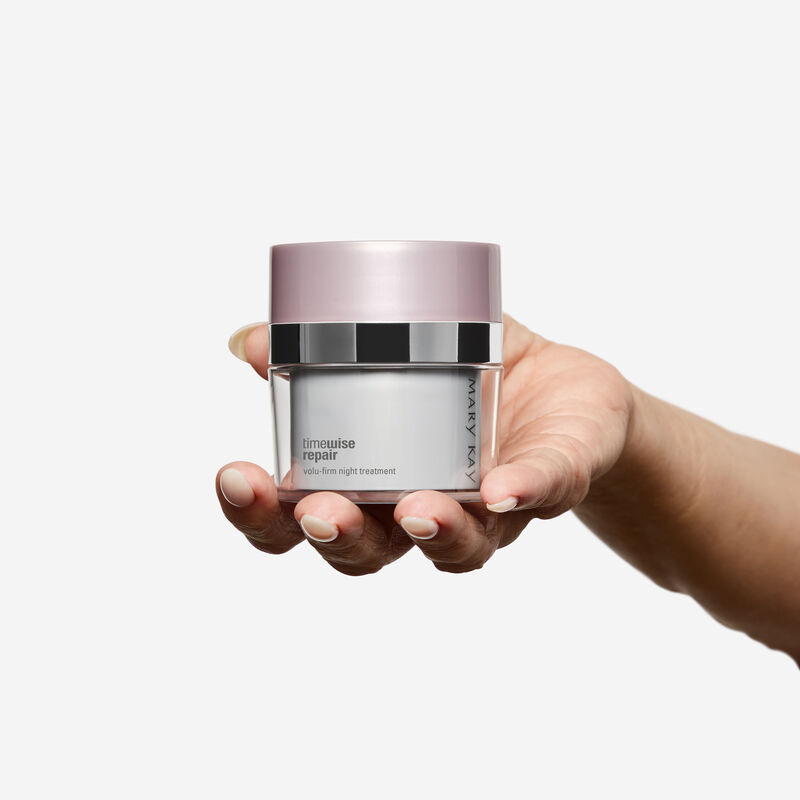 Fair-skinned hand holding Night Treatment jar on plain background.