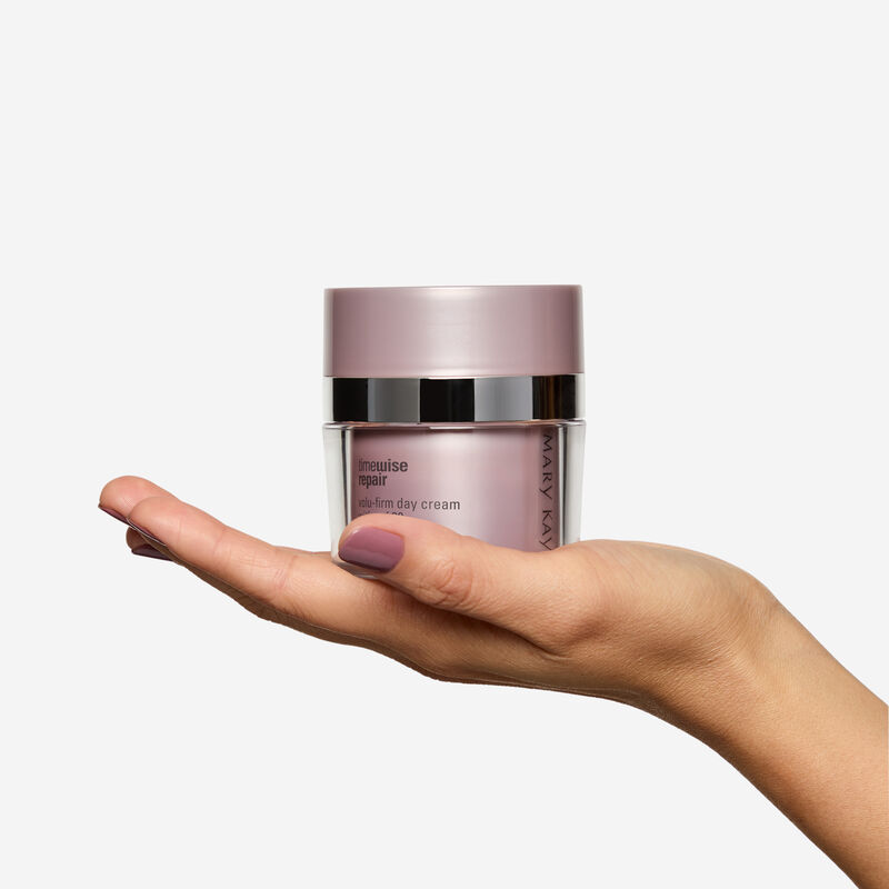 Fair-skinned hand holding Day Cream jar on plain background.