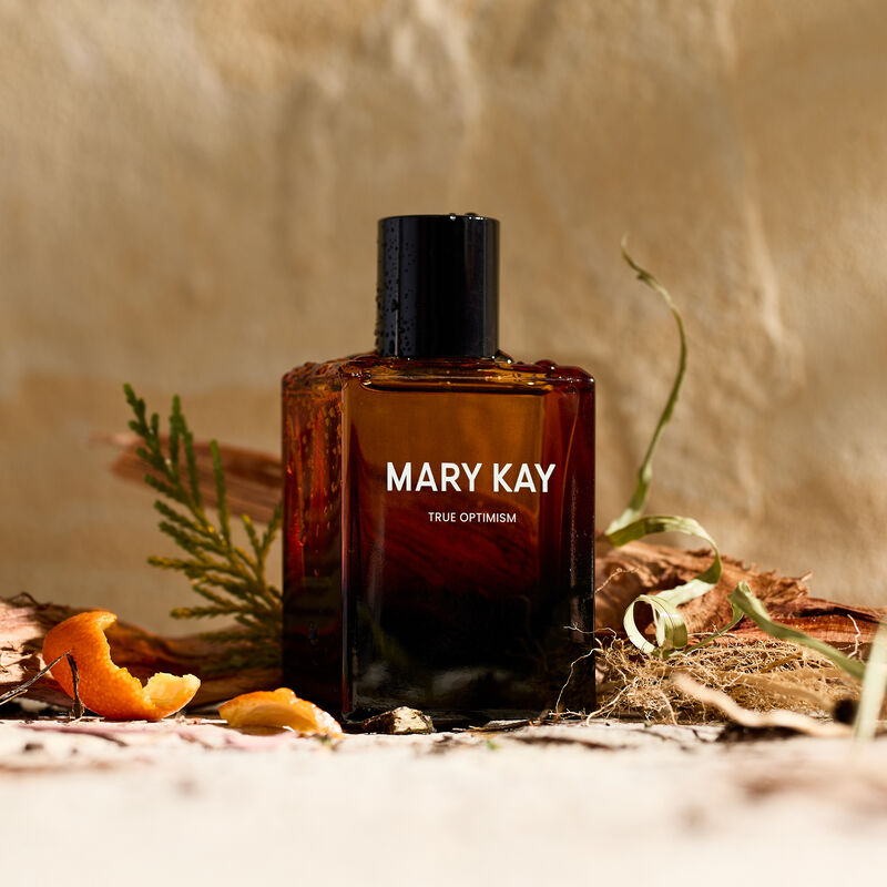 Mary Kay True Optimism Eau de Parfum surrounded by fragrance note ingredients, against stone background