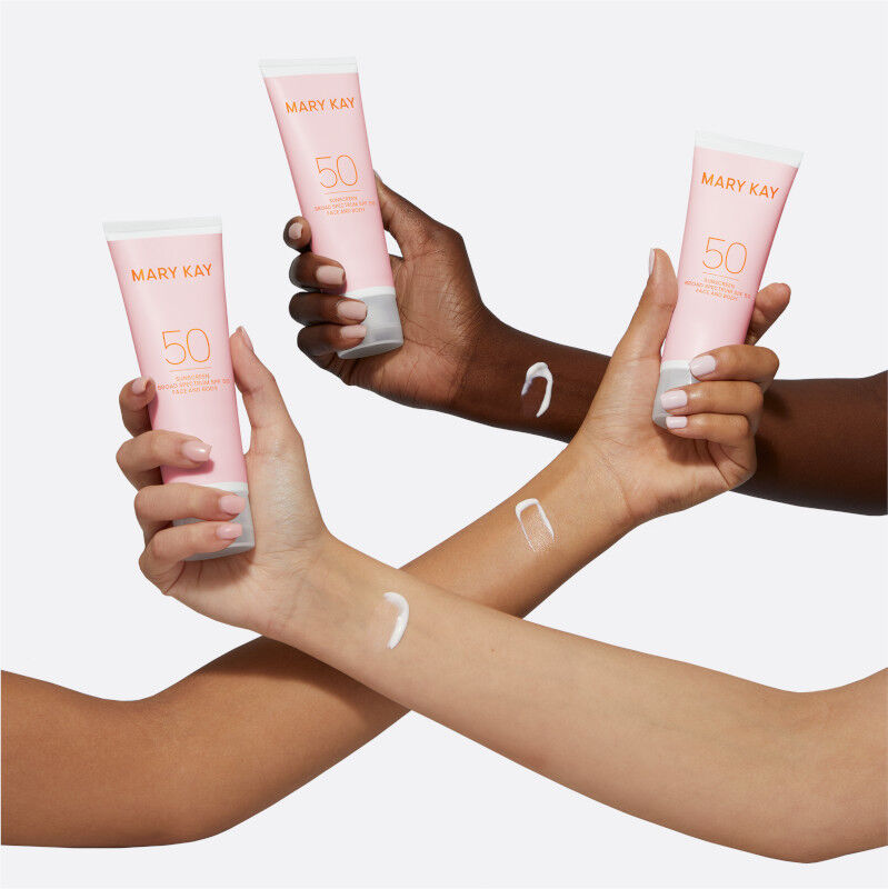 Light, medium and deep-skinned arms crossing, each with a sunscreen smear near wrist and holding a tube of Mary Kay Sunscreen Broad Spectrum SPF 50